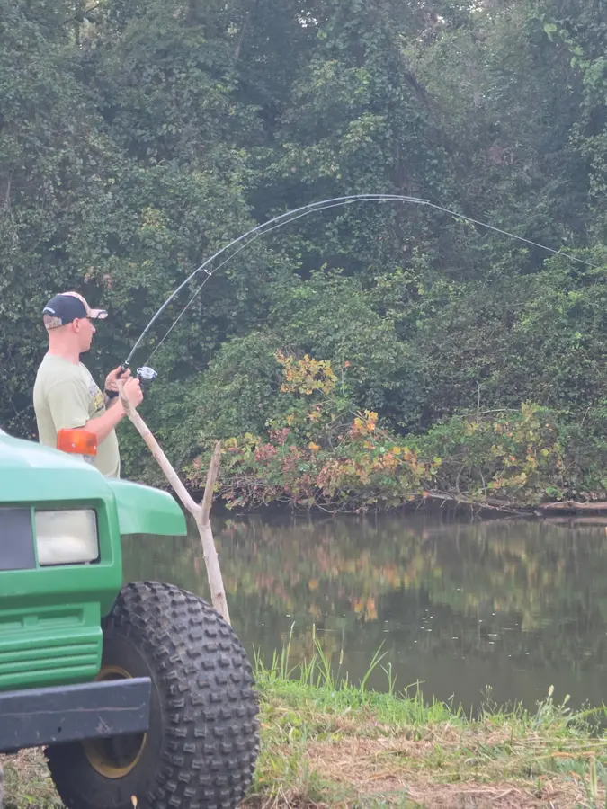 An angler on the bank with a bent fishing rod beside Yadkin River, enjoying great fishing and fun at Hillbilly Campground.
