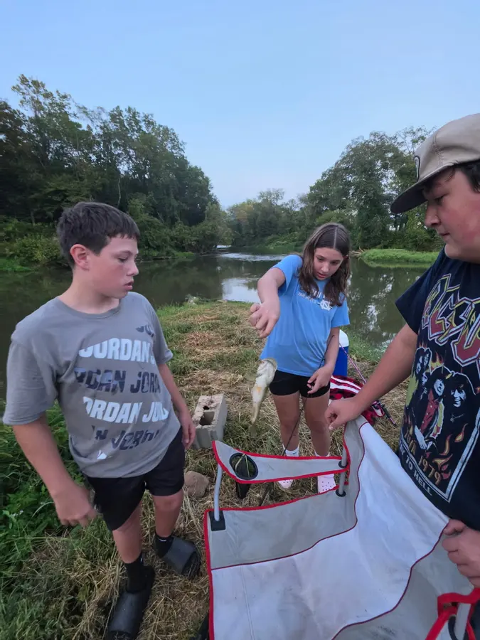 Two young anglers and an adult standing beside fishing gear on the bank of Yadkin River, sharing great fishing and fun at Hillbilly Campground.